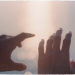 Abstract silhouette of hands reaching out towards soft sunlight, creating a dreamy effect.